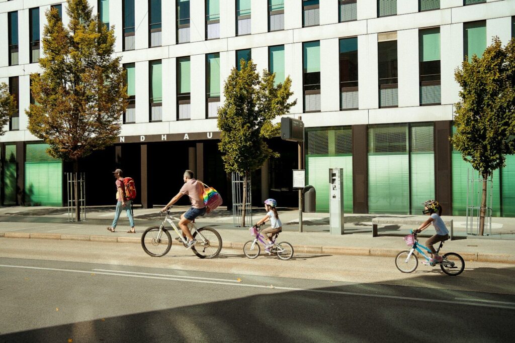 People cycling past a modern building on a sunny day.